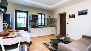 Een moderne keuken met witte kastjes, een eethoek met een tafel gedekt voor twee personen, en een zithoek met een bank en salontafel.