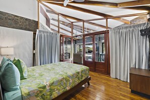 Ein Schlafzimmer mit Bett, Vorhängen, Holzboden und Blick ins Freie.