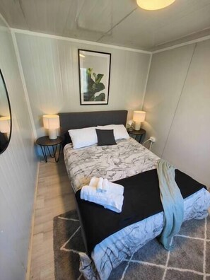 Een netjes opgemaakt slaapkamer met een bed, twee nachtkastjes, een wandspiegel en een lijst met een afbeelding.
