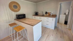 Une cuisine compacte avec un plan de travail en bois, des placards blancs, un four à micro-ondes et une machine à café. On y trouve deux tabourets et un petit évier.