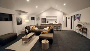 Un soggiorno moderno con divano, tavolino da caffè e poggiapiedi, una zona cucina e un'area pranzo.