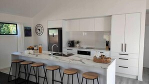 Una cucina moderna con un piano di lavoro in marmo, elettrodomestici in acciaio inossidabile e mobili bianchi. Quattro sgabelli di legno sono posti all'isola.