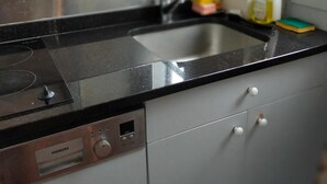 Et køkken med en sort bordplade, en stålvask og en Siemens hvidevare.