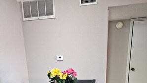 A dining area with a dark wooden table and four chairs, each with a cushioned seat. There are two potted plants with yellow and pink flowers on the table. - A Private Retreat Made for Extended Houston Stays (Houston)