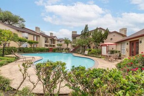 A pool surrounded by apartment buildings with outdoor seating and a landscaped garden.