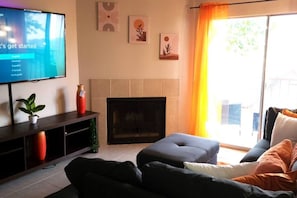 A living room with a flat-screen TV, a fireplace, a sofa, and a sliding glass door with curtains.