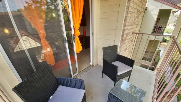 A balcony with wicker furniture and a glass table. - A Private Retreat Made for Extended Houston Stays (Houston)