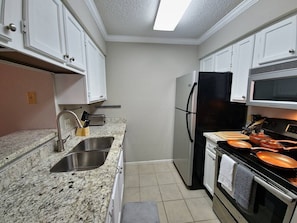 A compact kitchen with white cabinets, a stainless steel sink, a black refrigerator, and a stove with copper pans.