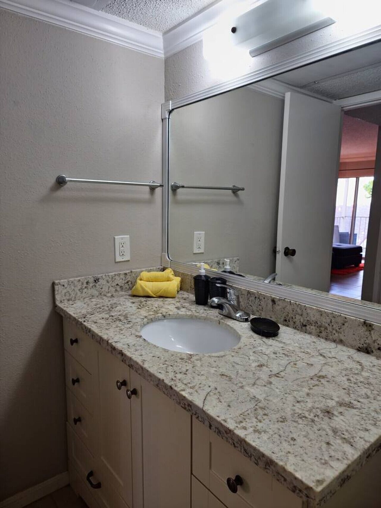 A bathroom with a granite countertop sink, a mirror, and a towel rack.