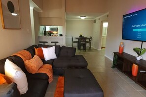 A modern living room with a sectional sofa, a flat-screen TV, and a dining area in the background. - A Private Retreat Made for Extended Houston Stays (Houston)