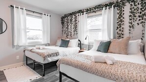 Un dormitorio con dos camas, ropa de cama blanca, una alfombra pequeña y una ventana con cortinas.