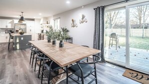 Una cocina moderna con armarios blancos, una mesa de comedor de madera y sillas negras. Hay un ventanal con vistas al jardín trasero.