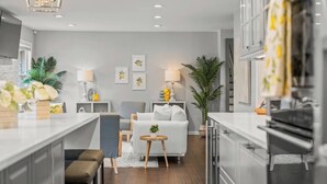 A modern kitchen with a central island, grey upholstered seating, and a dining area. - Zestlife-HeatedPool-LuxeEscp-ThemedRooms-GameRoom (Indianapolis)
