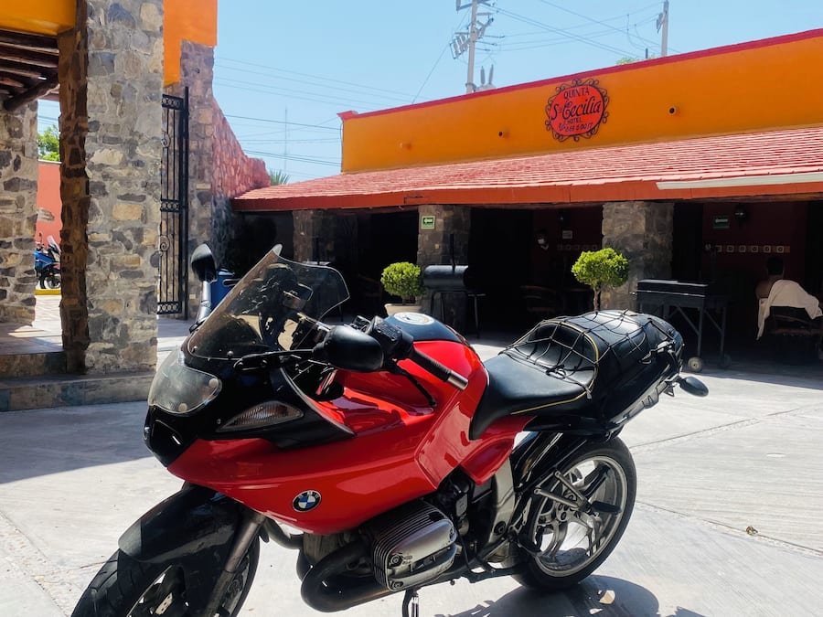 A red BMW motorcycle parked in front of a hotel with a stone pillar and a red roof.