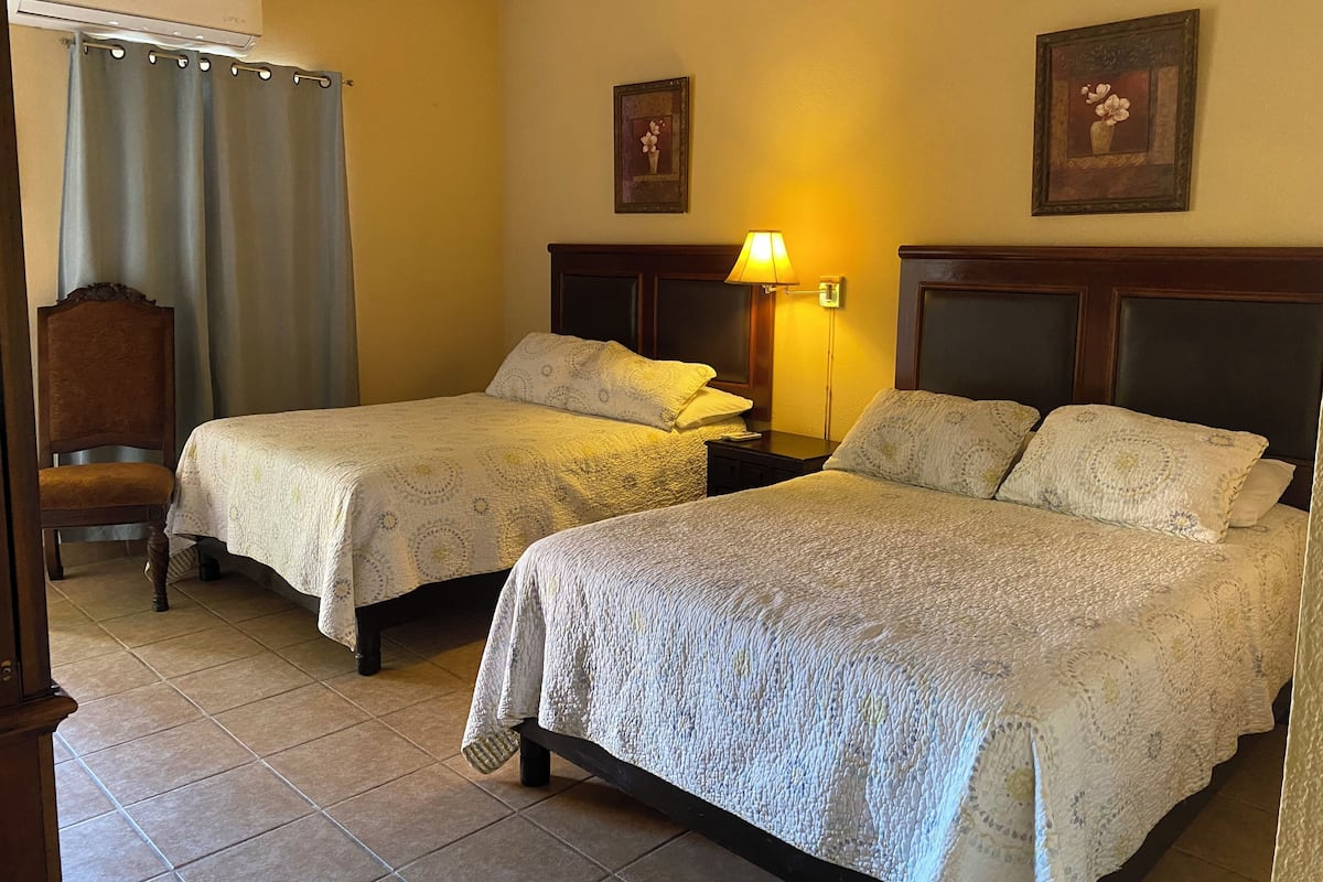 Habitación de hotel con dos camas, una silla, una lámpara y un cuadro en la pared.