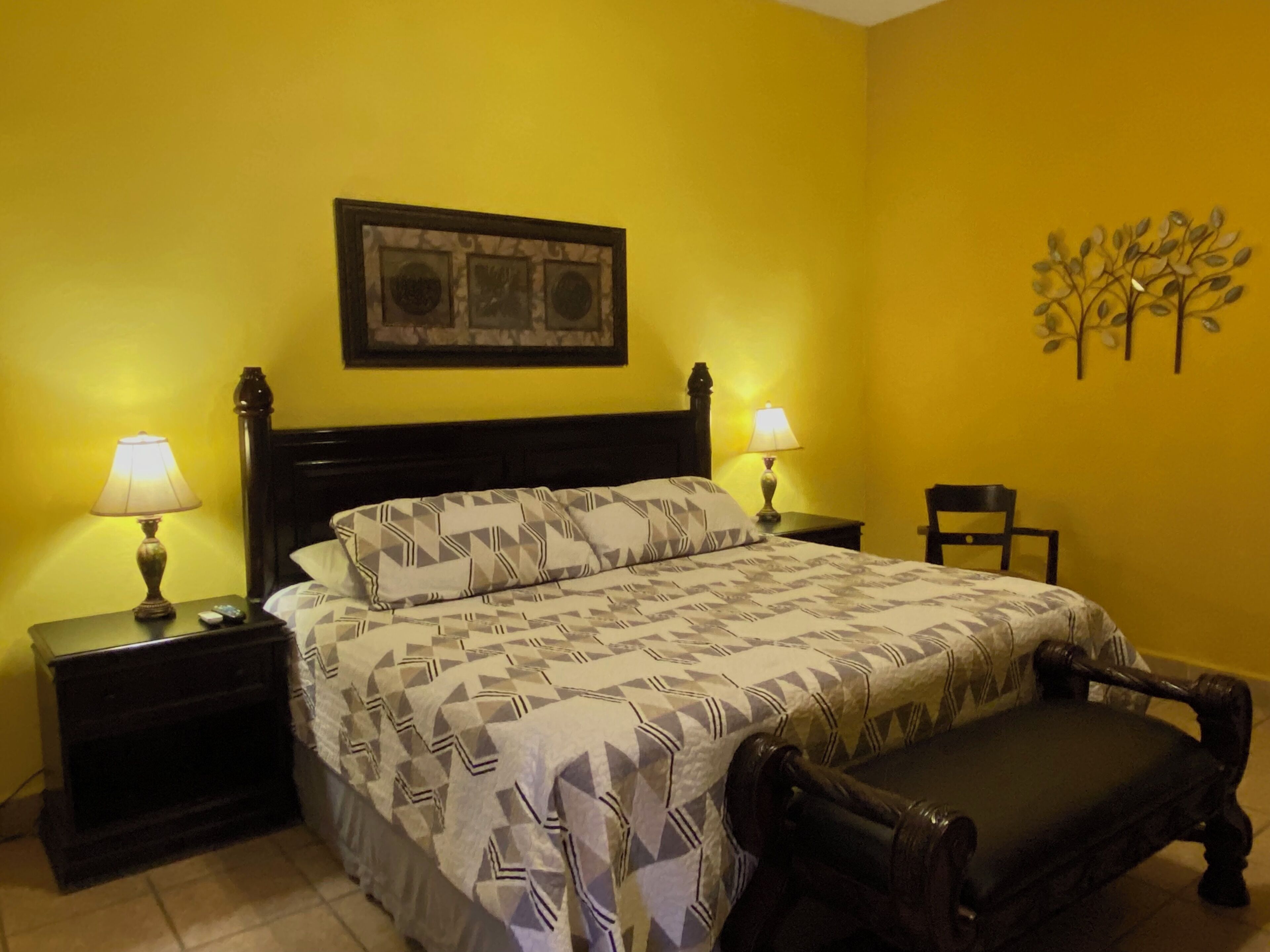 Une chambre à coucher comprenant un lit, deux tables de chevet avec des lampes, une chaise et un élément décoratif fixé au mur.