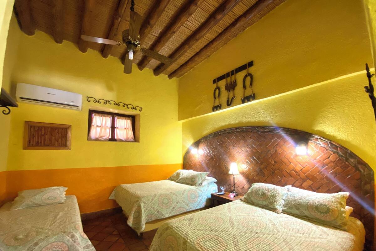 Una habitación con dos camas, techo de madera, pared de ladrillo y aire acondicionado.