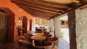 An outdoor dining area with wooden tables and chairs, stone walls, and a thatched roof. - Hotel Quinta Sta Cecilia (Cuatro Ciénegas)