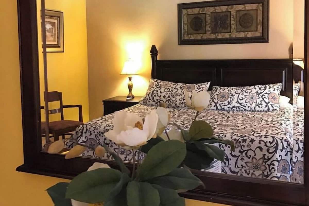 Una habitación de hotel con una cama, una mesita de noche, una lámpara, una silla y un espejo.
