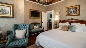 Quarto com cama grande, poltrona estofada, cabeceira de madeira e lustre.