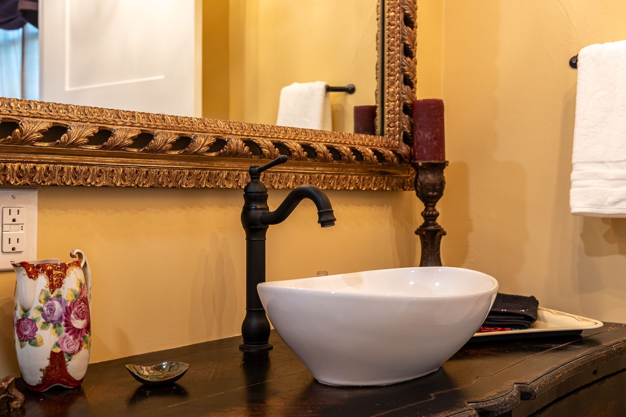 A bathroom with a white sink, a decorative pitcher, a small dish, and a mirror with an ornate frame.