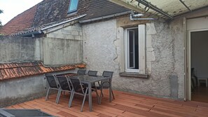 Una terrazza esterna con tavolo e sedie, una finestra con persiane e un tetto in tegole.