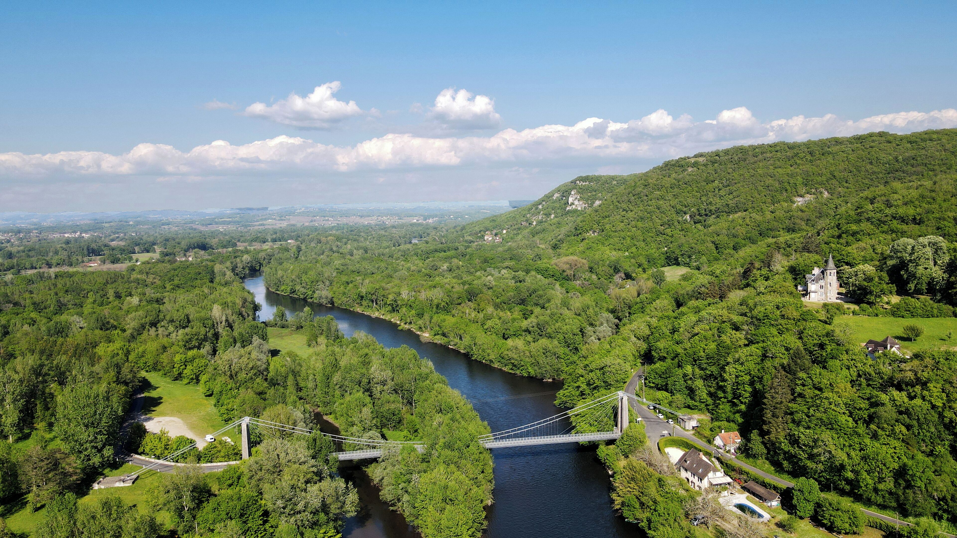Un río serpentea por un valle exuberante, con un puente y una estructura que parece un castillo en una colina.