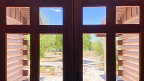 A set of wooden doors with multiple windows, each revealing a view of a landscaped outdoor area with trees and a stone pathway. - Lodge II | Lake Views | Hot Tub | Pool + River Access (Ingram)