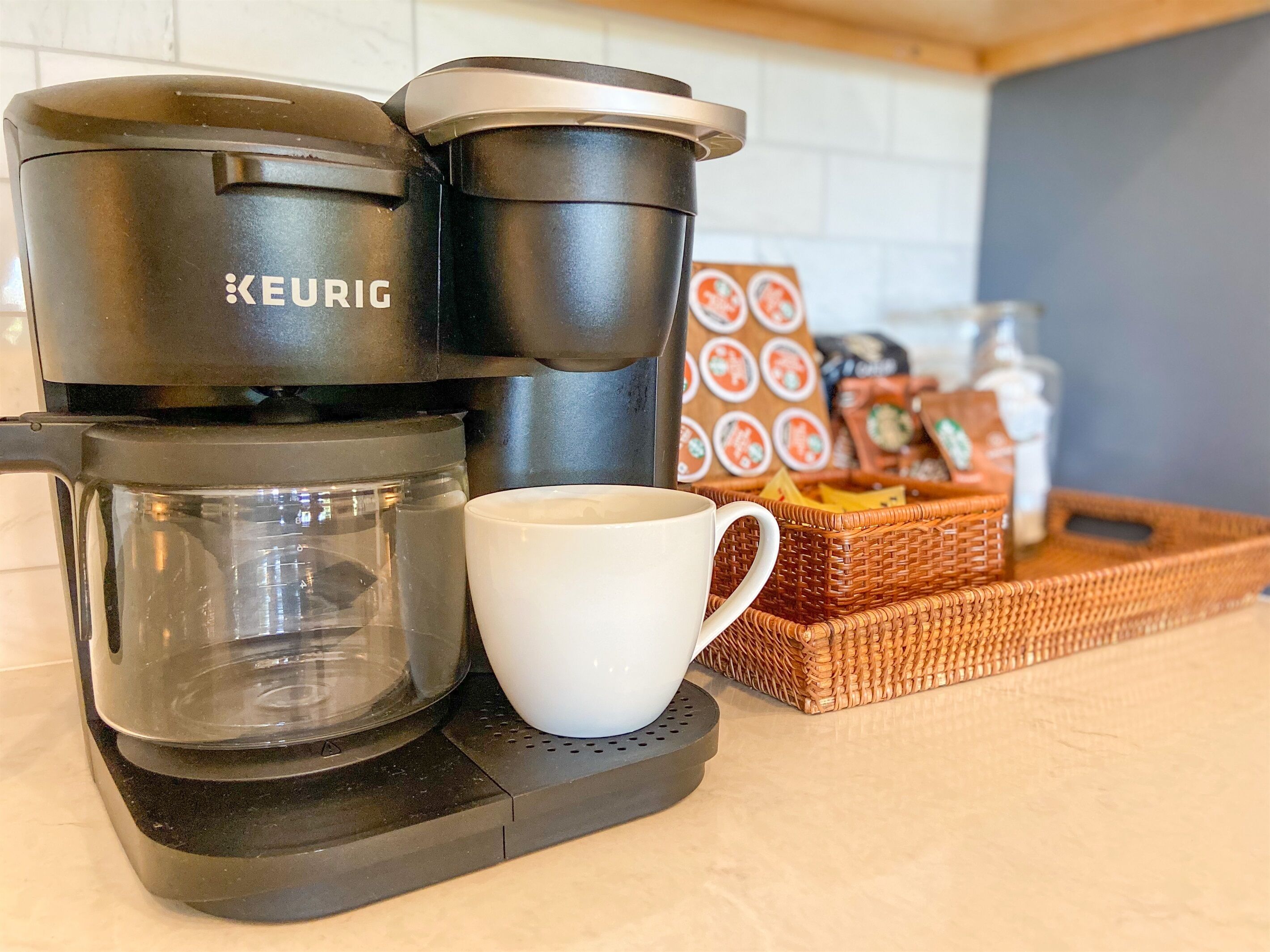 A Keurig coffee maker with a glass carafe and a white mug on a kitchen counter.