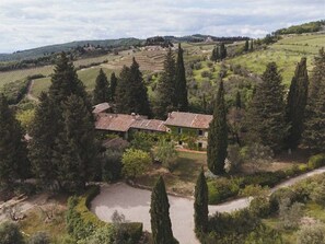 Uma propriedade rural com campos em socalcos, um edifício principal com telhado de cerâmica e altas árvores de cipreste ao redor.