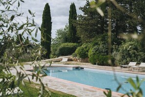 Piscina com borda de pedra, cercada por vegetação exuberante e árvores altas.