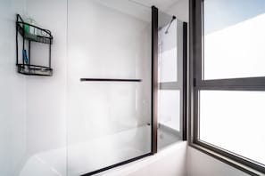 A modern bathroom with a glass shower enclosure, a towel rack, and a window providing natural light.