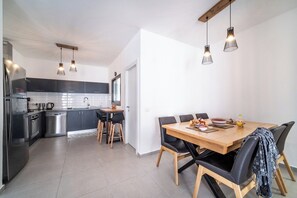 Une cuisine moderne dotée d’appareils électroménagers en acier inoxydable, un coin repas avec une table en bois et des chaises noires, et un éclairage suspendu.