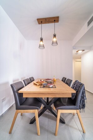 Un espace repas avec une table en bois, des chaises en cuir noir et des luminaires suspendus.