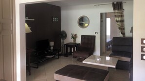 Una sala de estar con sofá, sillón, televisor y un reloj en la pared.