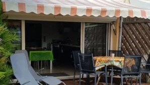 Un espacio de estar al aire libre con techo, una mesa y sillas, una entrada con puerta corredera de vidrio y una valla de madera.