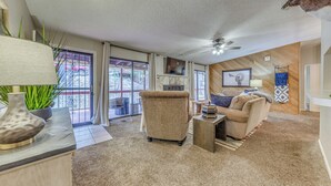 A cozy living room with a sofa, armchair, and a coffee table. There is a ceiling fan, a fireplace, and a large window with a view of the outside. - 1 Mi to Ski Slopes: Alto Escape w/ Game Room! (Alto)