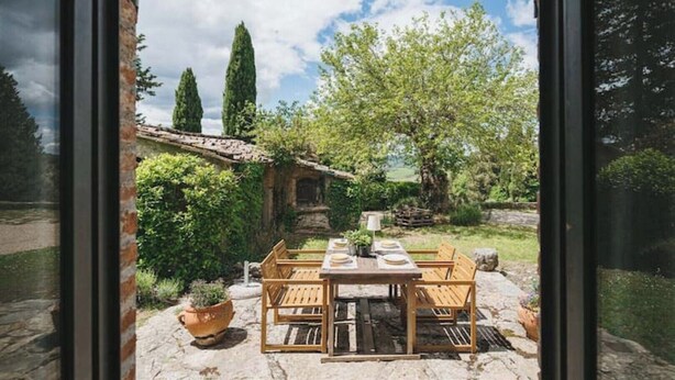 Une terrasse avec une table dressée pour quatre personnes, entourée d’un sol en pierre et de plantes en pot.