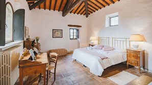 Une chambre avec un plafond en bois, un lit avec une literie blanche, une table de chevet avec une lampe, une commode en bois et une fenêtre.