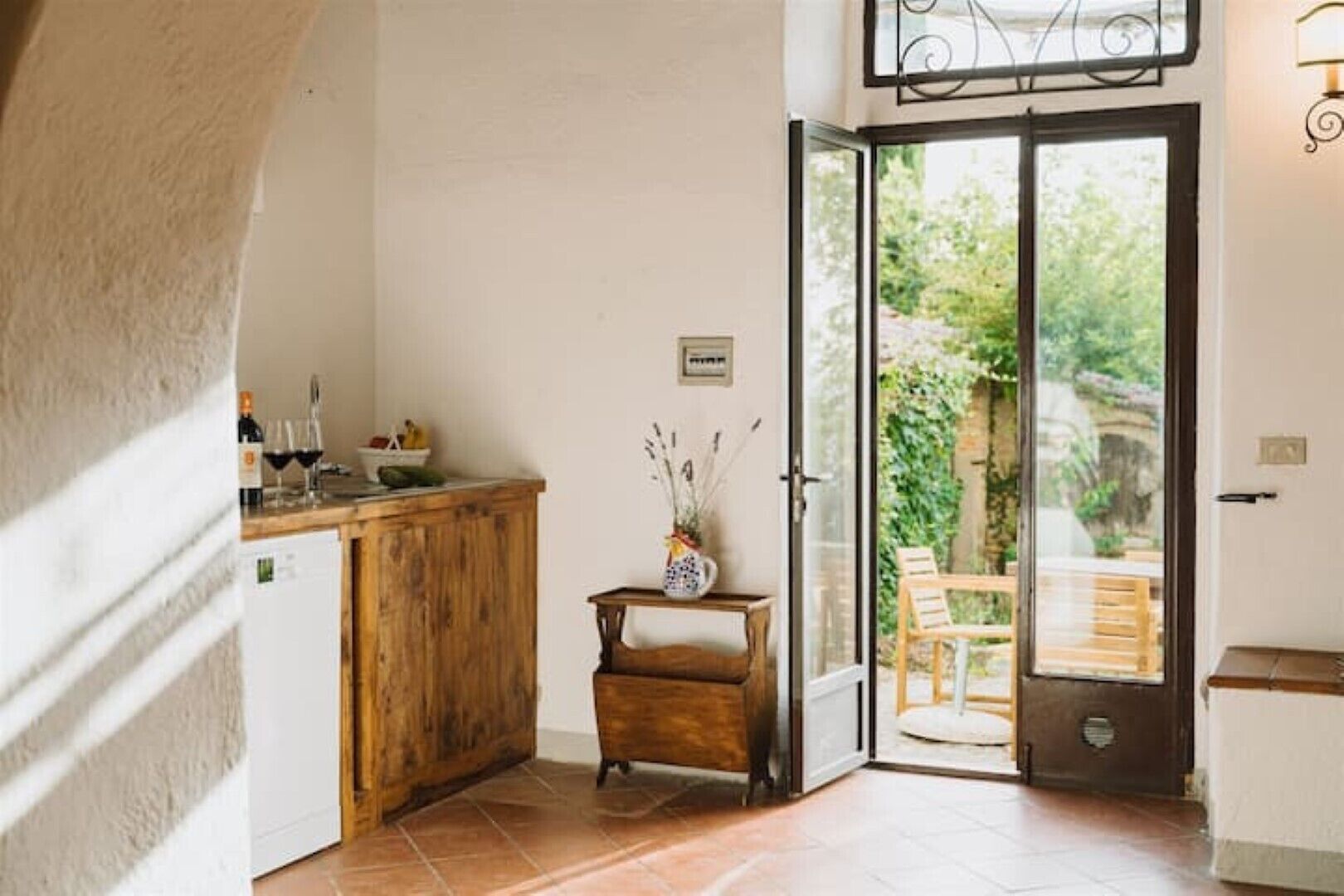 A kitchen with a wooden counter, a small table with a vase, and a sliding glass door leading to an outdoor seating area.