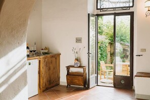Una cocina con mostrador de madera, una mesita con un florero y una puerta corrediza de vidrio que da a una zona de estar exterior.