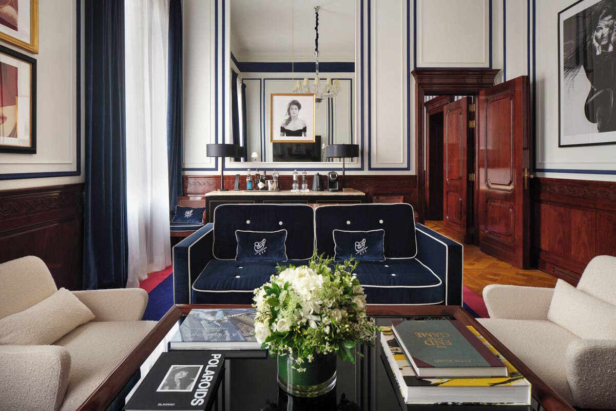 A formal room with a large sofa set, a coffee table with books and a vase of flowers, a chandelier, and a mirror.