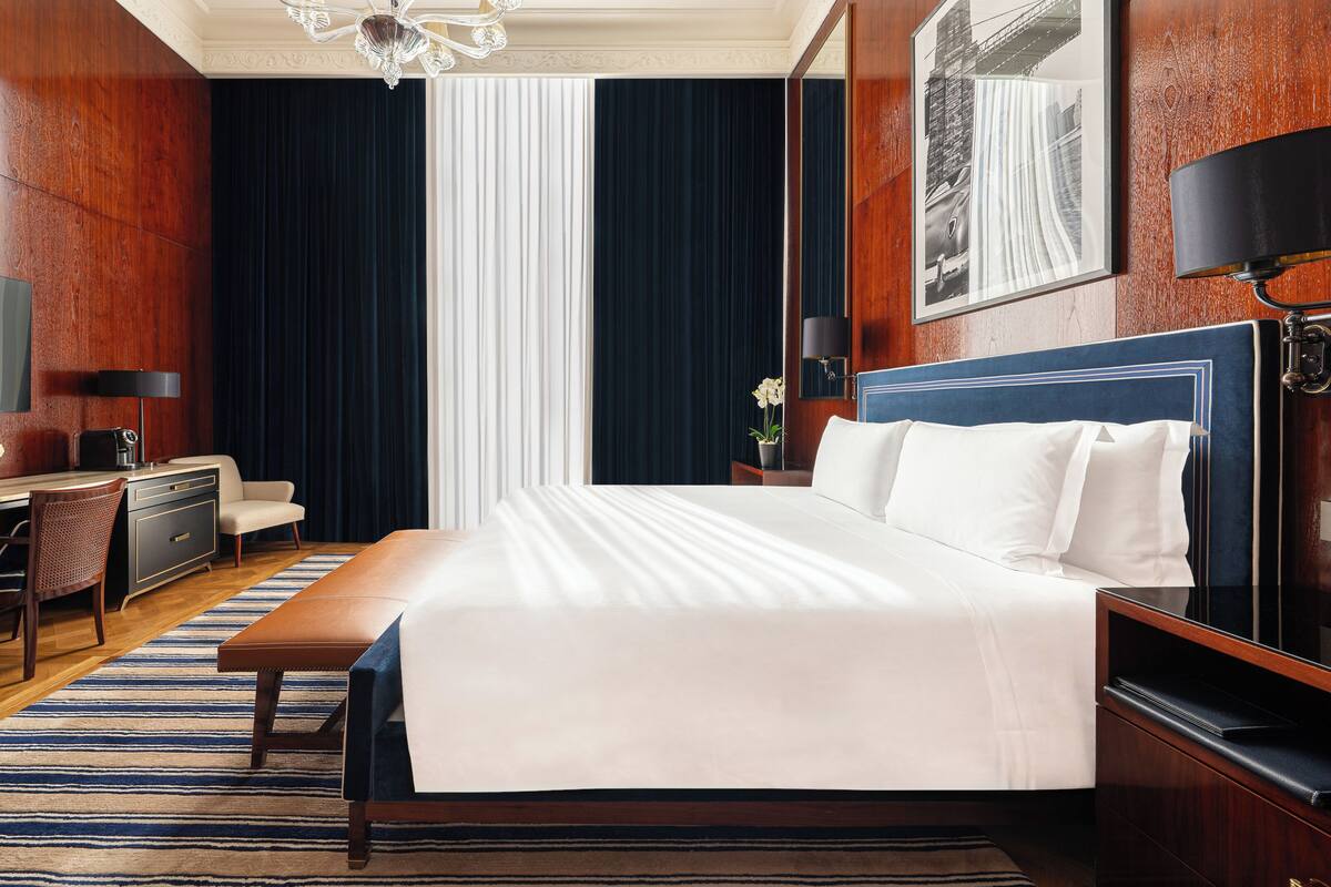 A hotel room with a large bed, a desk with a chair, a TV, and a window with curtains.