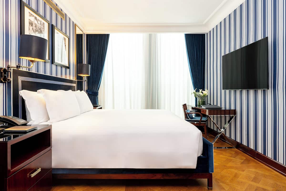 A hotel room with a large bed, a desk with a chair, a flat-screen TV, and a telephone on the nightstand.