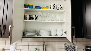Une cuisine avec des étagères blanches où sont rangées de la vaisselle, des tasses et des verres.