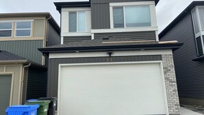Une maison à deux étages avec un portail de garage, une boîte aux lettres et deux poubelles.