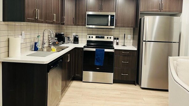 Une cuisine moderne avec des meubles en bois foncé, des appareils électroménagers en acier inoxydable et un plan de travail blanc.