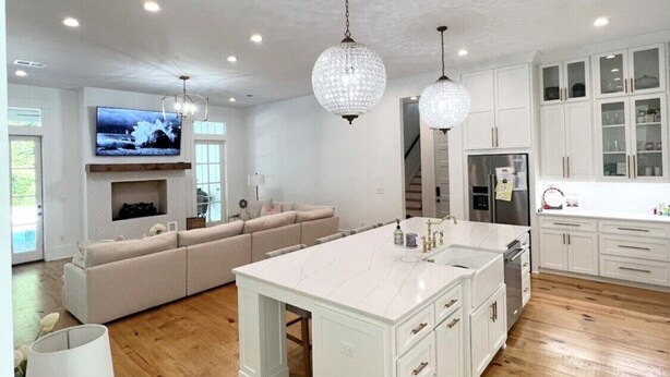 Una cocina amplia con una isla grande, armarios blancos e iluminación colgante.