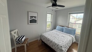 Un dormitorio con cama, ventilador de techo, ventana y una silla.