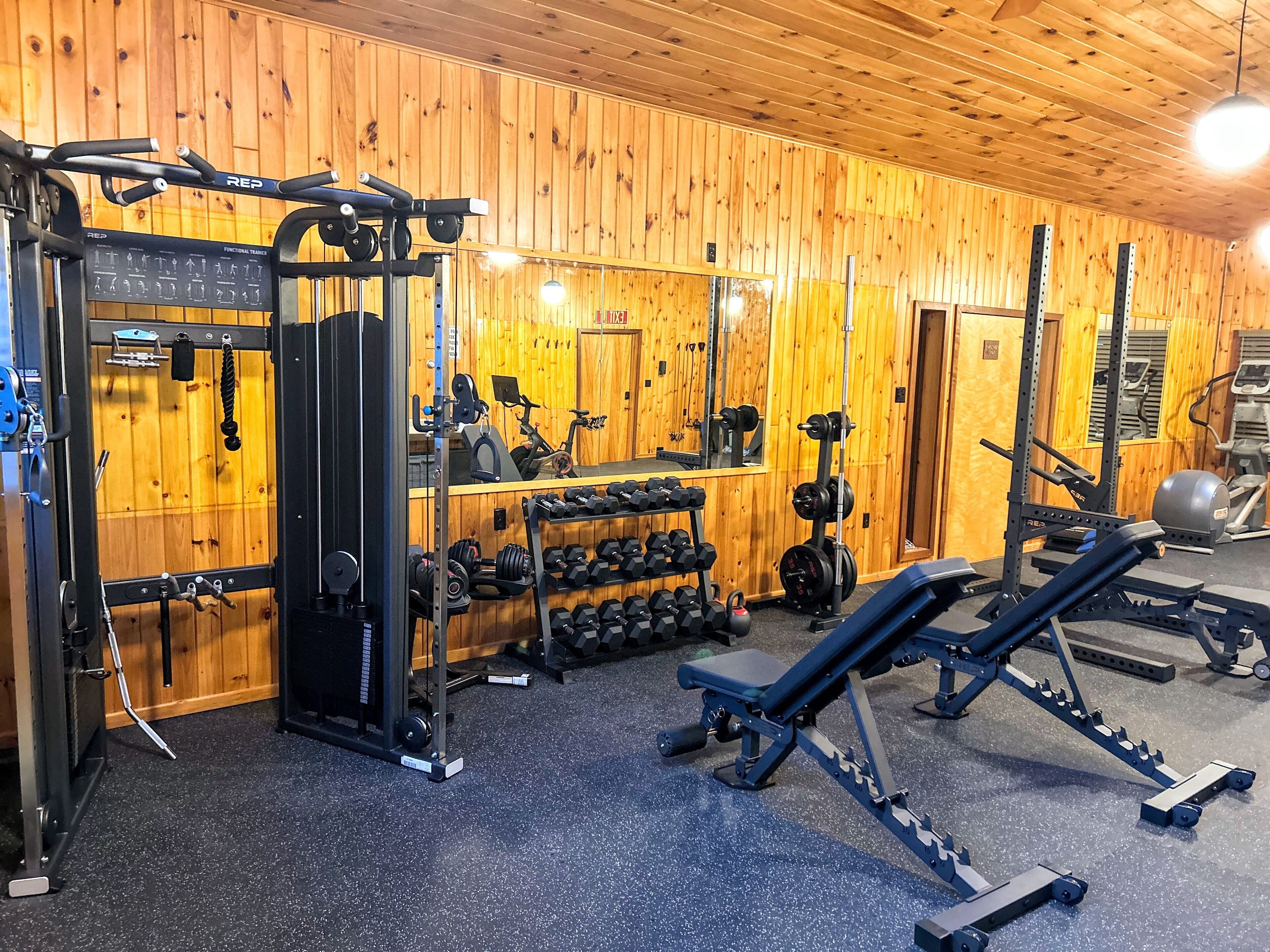 Uma academia com paredes de madeira, diversos equipamentos de ginástica e um espelho.